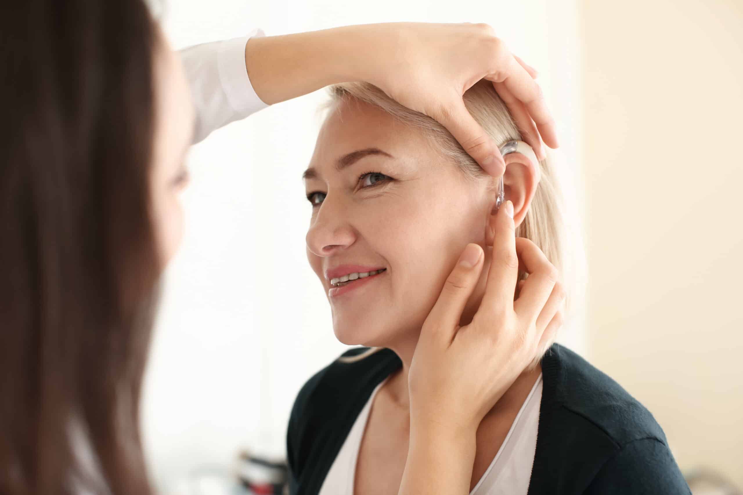 Otolaryngologist,Putting,Hearing,Aid,In,Woman's,Ear,On,Light,Background oticon demant hearing health
